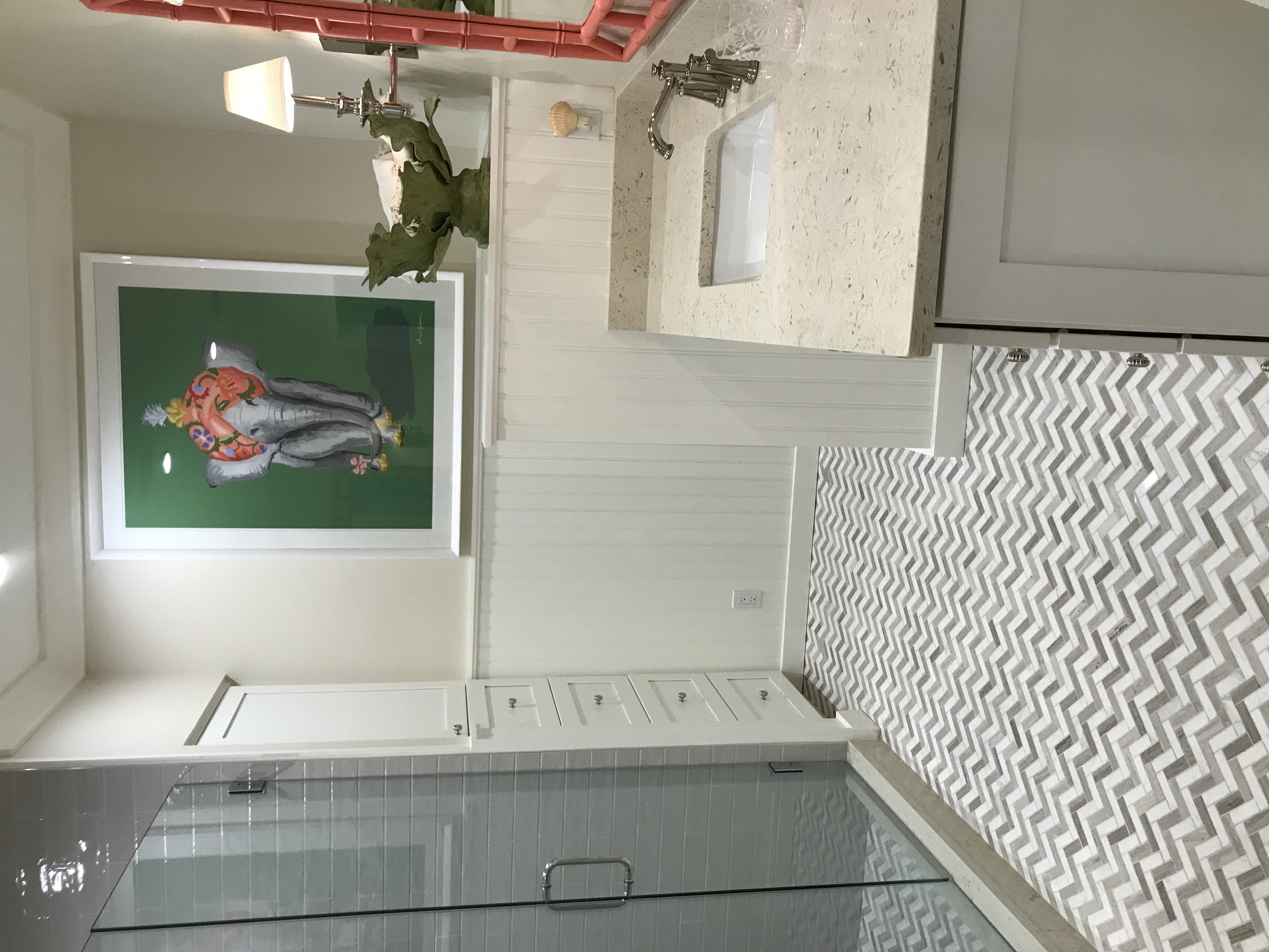 Remodeled bathroom with patterned stone floor, custom vanity, glass shower, and colorful artwork