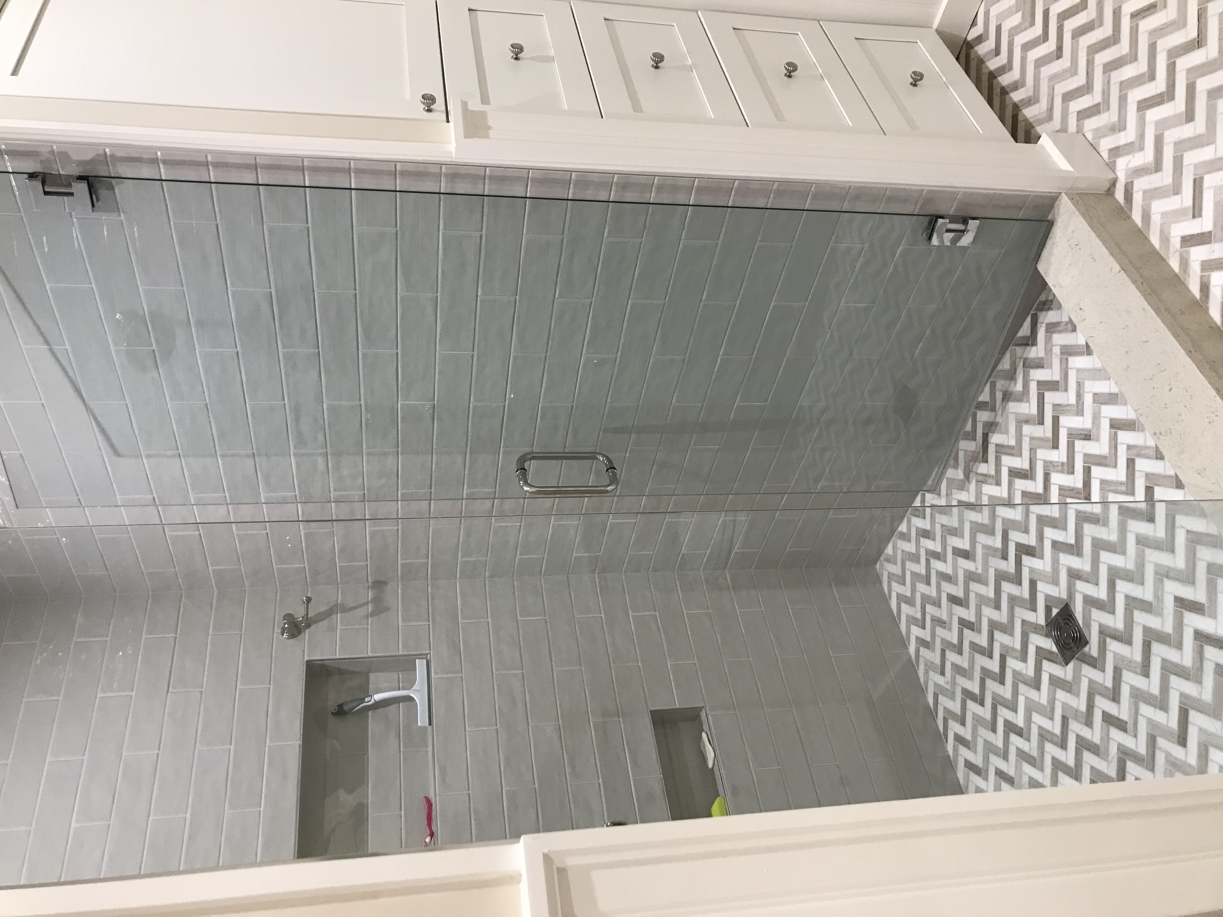 Frameless glass shower with gray tile, recessed storage, and patterned stone floor