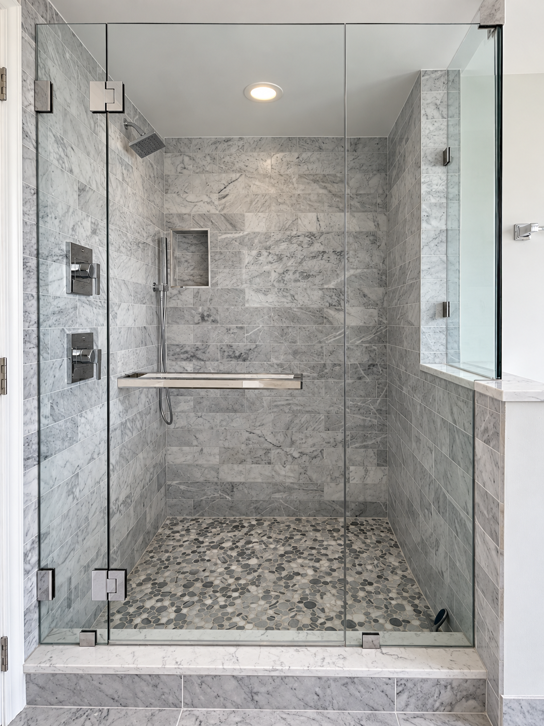 Frameless glass shower with marble tile, pebble-stone floor, and recessed niche